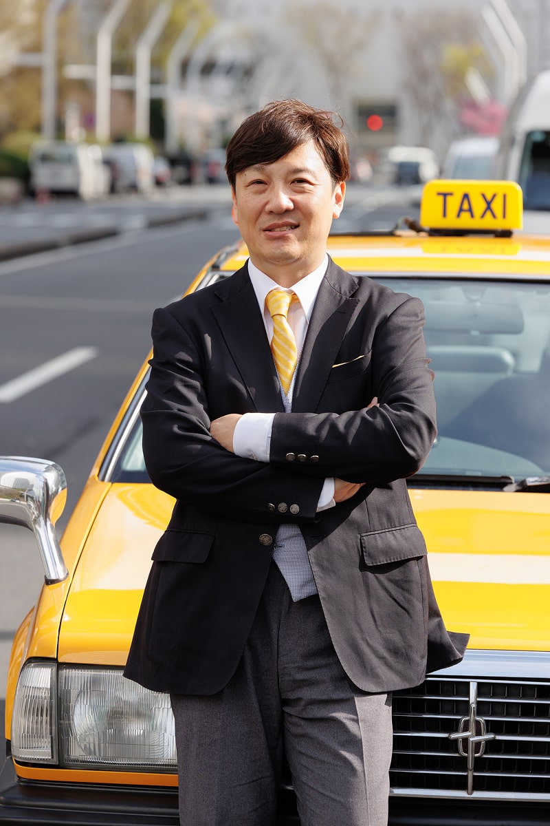 黄色のタクシノー前で腕を組むタクシー運転手
