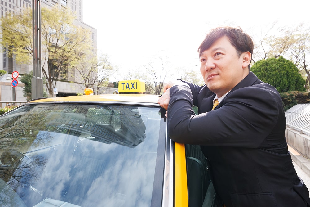 笑顔で車の窓から顔を出すスーツ姿のタクシー運転手