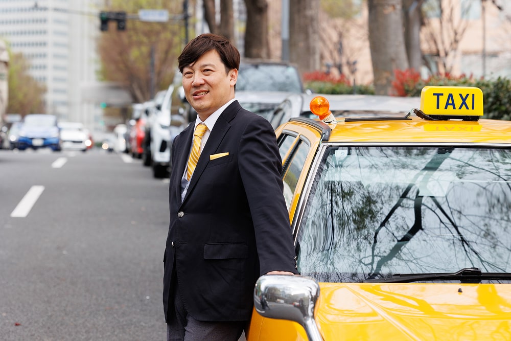 ハンドルを握って運転する笑顔のスーツ姿のタクシー運転手