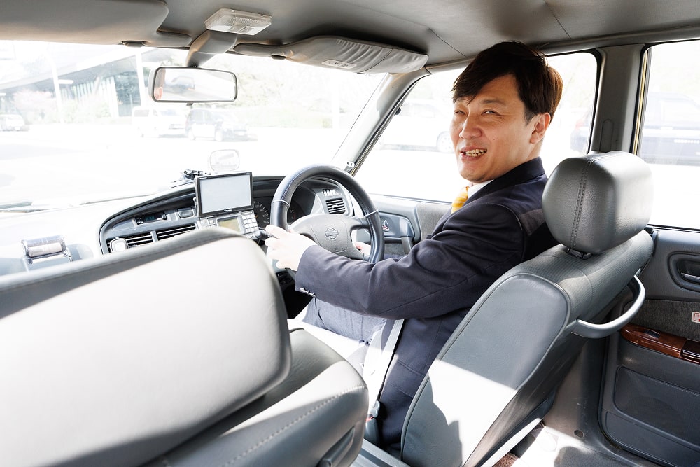 笑顔で車の窓から顔を出すスーツ姿のタクシー運転手