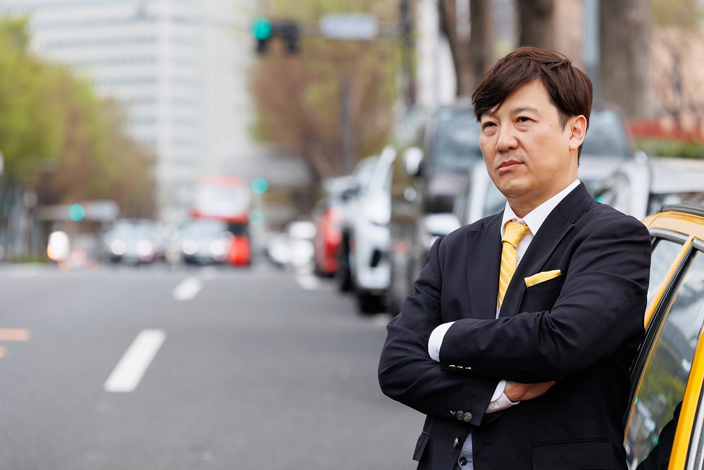 ハンドルを握って運転する笑顔のスーツ姿のタクシー運転手
