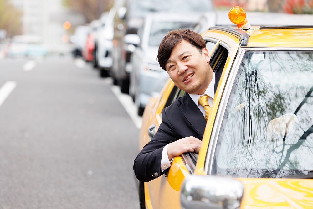笑顔で車の窓から顔を出すスーツ姿のタクシー運転手