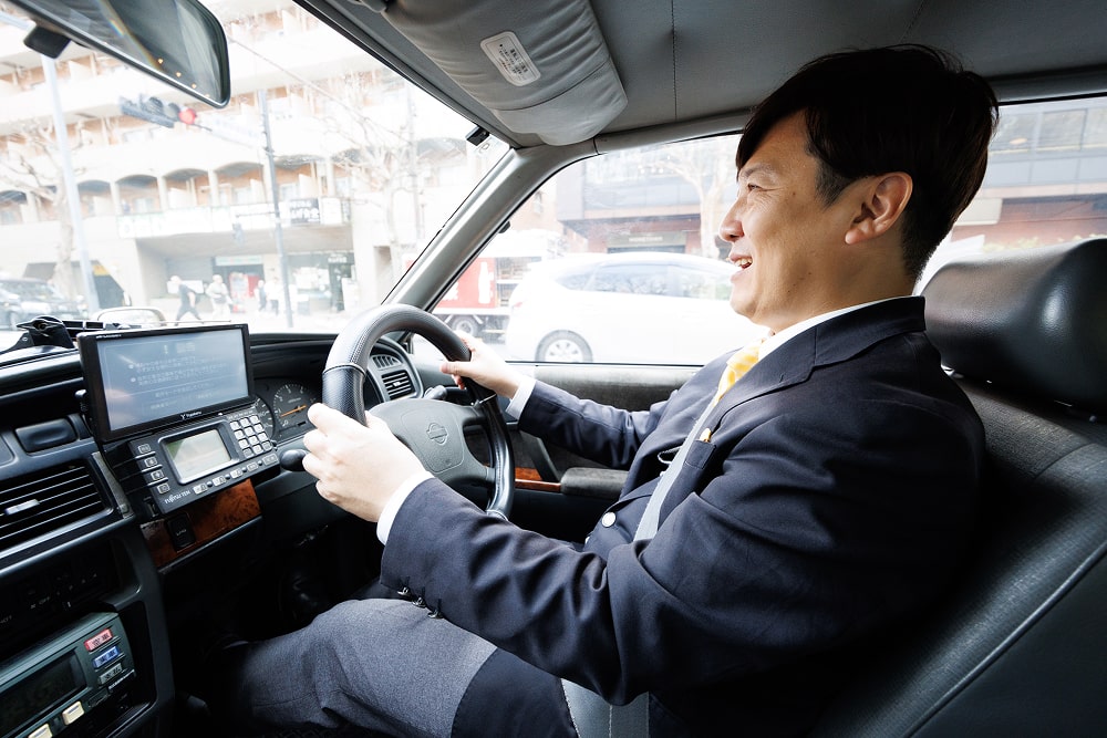 ハンドルを握って運転する笑顔のスーツ姿のタクシー運転手